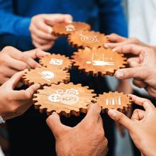 A diverse group of professionals collaborates using wooden cogs as symbols of business metrics and success in a modern office setting, highlighting teamwork and strategy.
