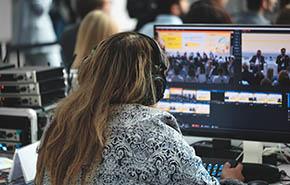 Woman wearing headphones sits in front of computer monitor. She's working on project or controlling audio and video during presentation.